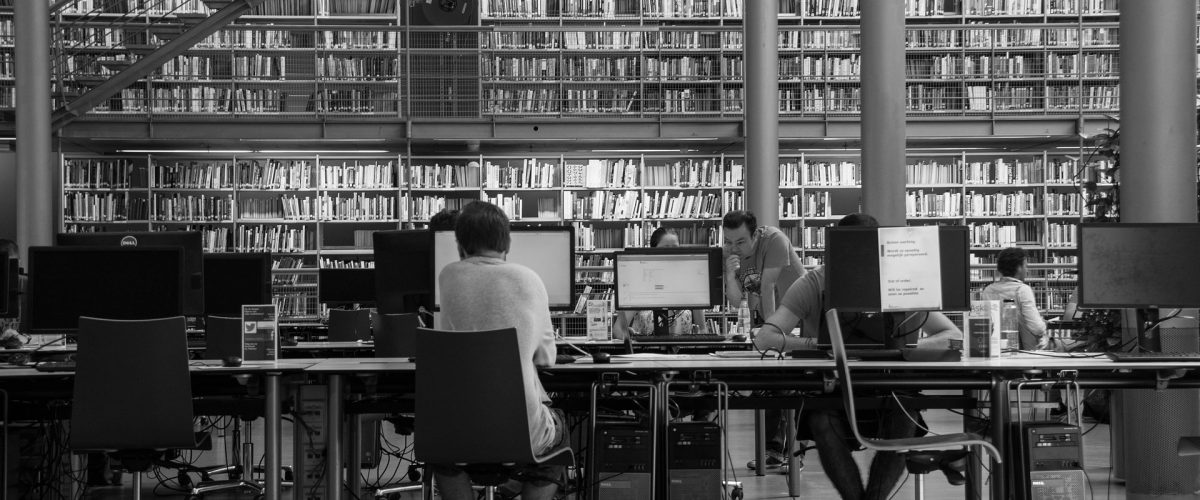A black and white photo of people working at computers in a library.